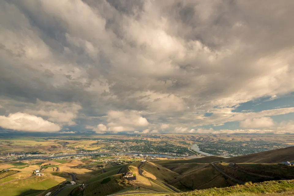 Distant view of Lewiston, Idaho nestled in green hills against cloudy blue sky